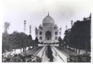 A black and white image of the Taj Mahal taking from the end of a rectangular pool. Trees flank either side.