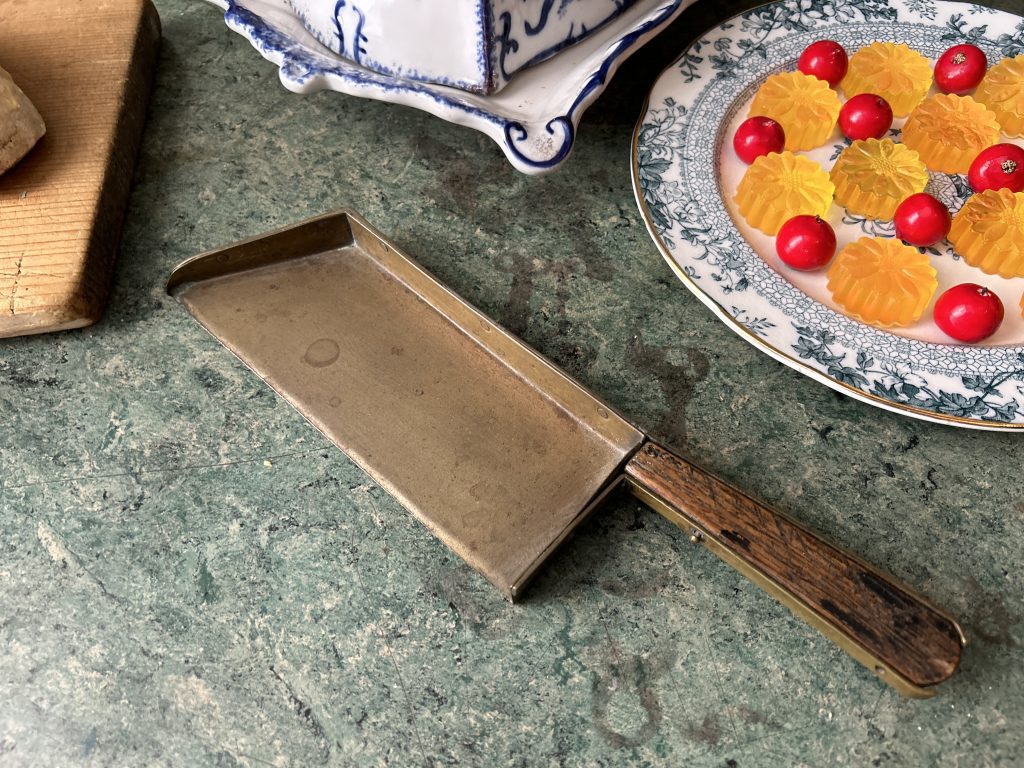 This is a metal crumb sweeper with a brown wooden handle. It is sitting on top of a green counter.