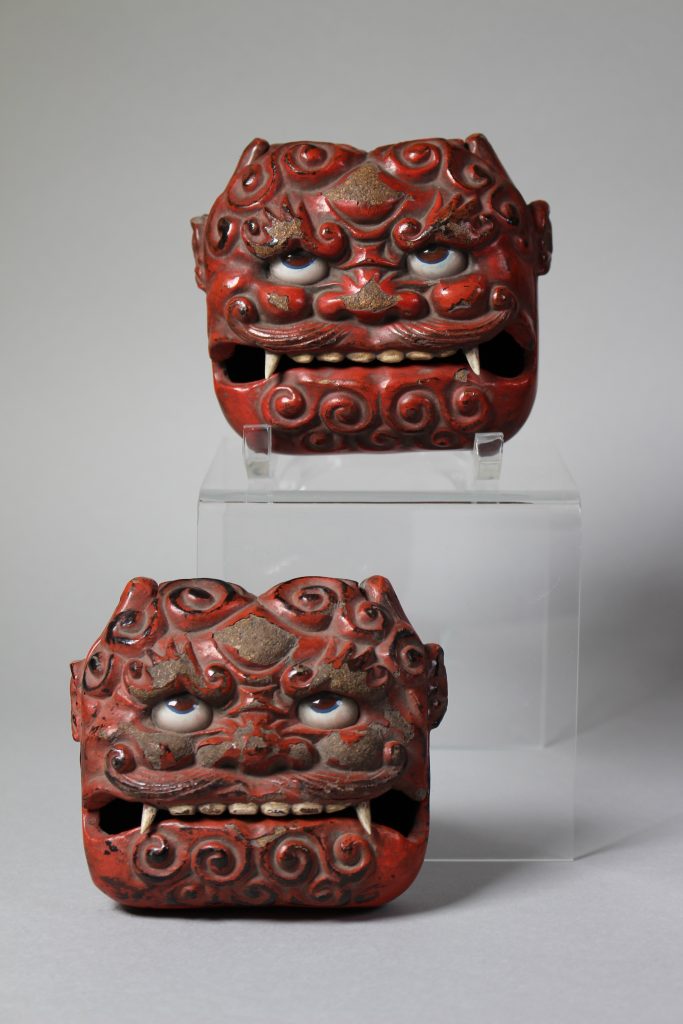 An image of the heads of two monsters. They are red with swirl patters. The eyes are white and made of glass, with brown pupils looking up. Their mouths are slightly open and pointy teeth are visible.