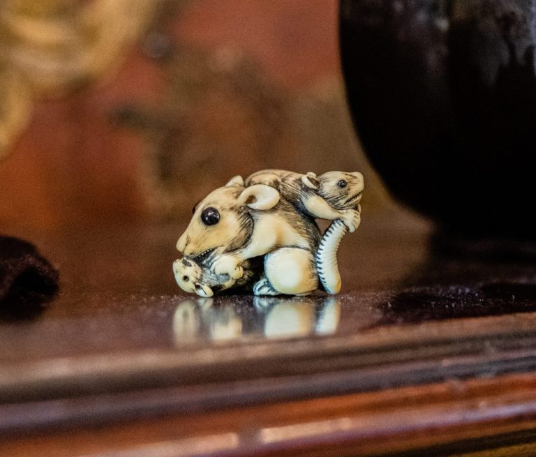 This is a three rat netsuke which depicts a figure of three white rats. It is placed on a wooden surface.