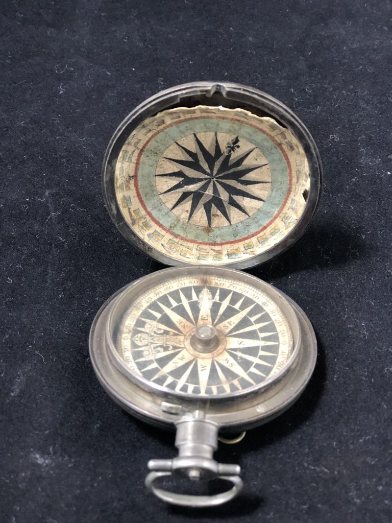 This is an image of an open compass. The face of the compass has all the directions in a star pattern. The other side has a star pattern that is surrounded green and red.