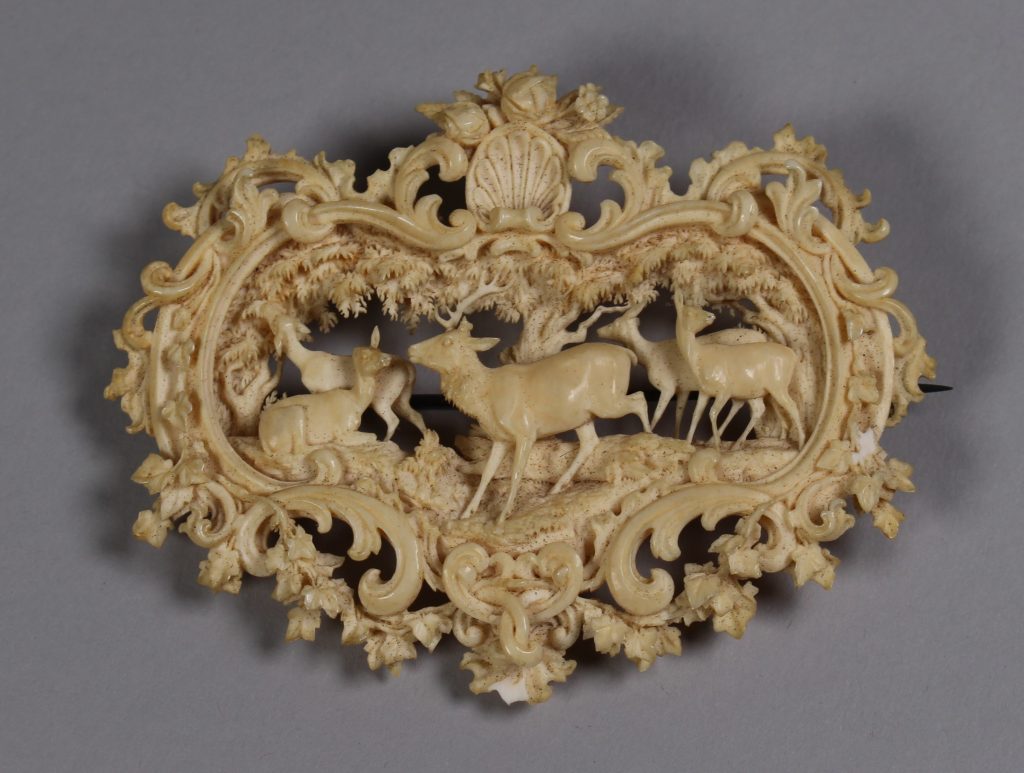 An image of a heart shaped brooch. Inside there are deer and florals on the outside.