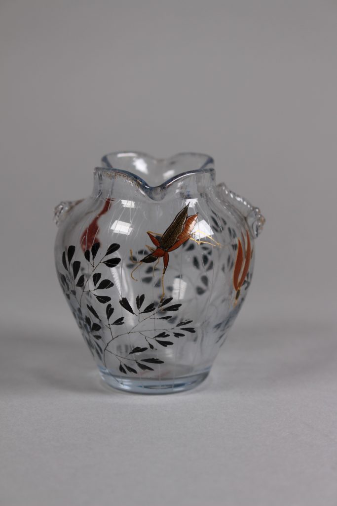 An image of a small glass that is curved at the top and tapers toward the bottom. On the glass are black leaves and a pattern of fish and bugs in orange.