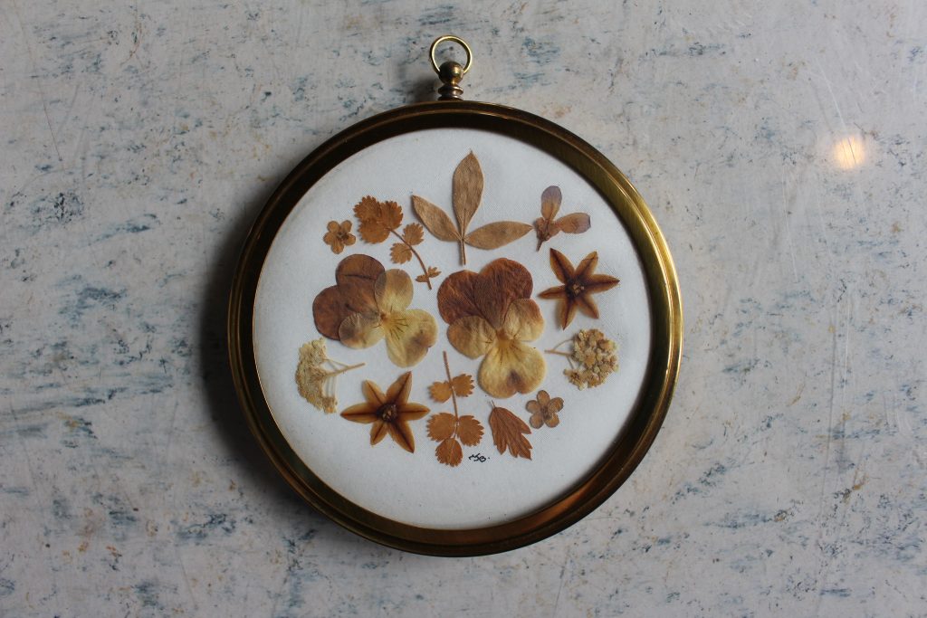 An image of a circular picture frame with some small brown flowers and leaves inside.
