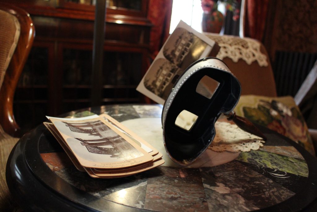 A pair of goggles with a double picture of Eldon House attached. There are a stack of images next to them, it is sitting on a multi-coloured table.