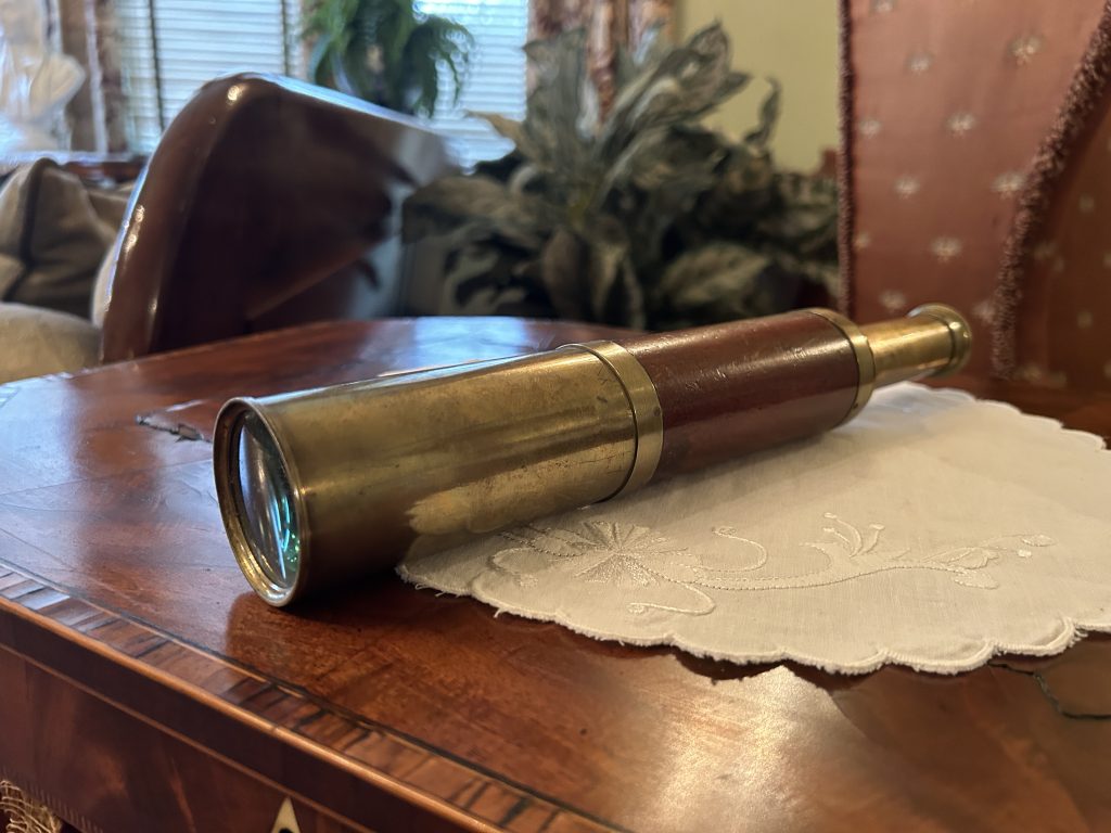 A long brass spy glass. It is sitting on a white doily on a wooden table.