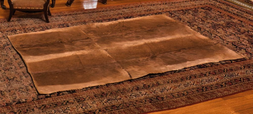 A hide rug that is striped beige and brown. It is sitting on a larger patterned rug.