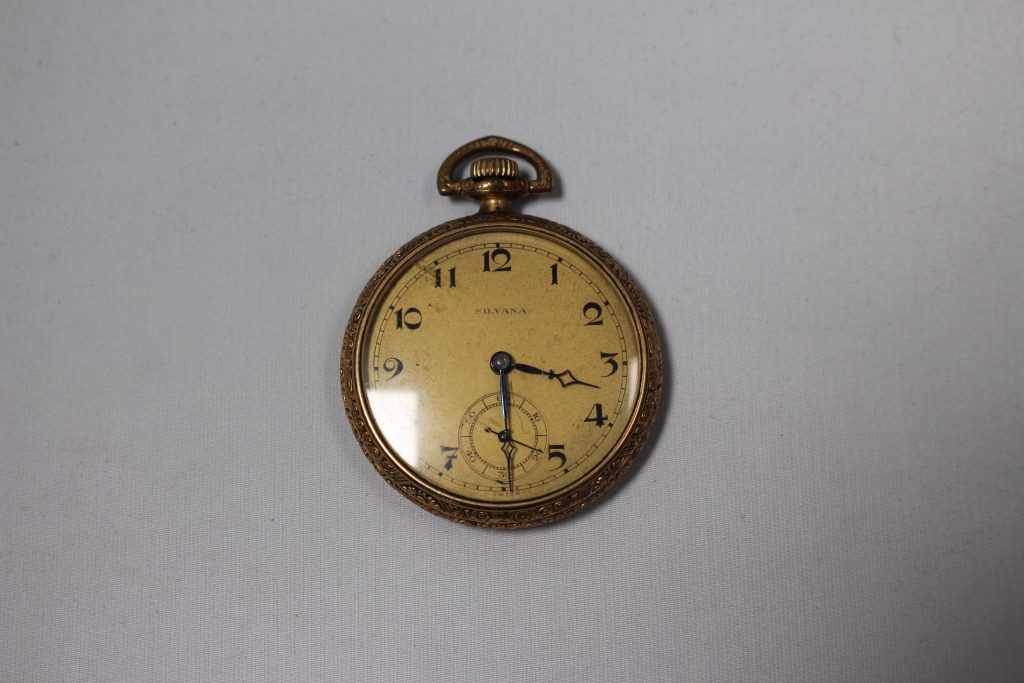 An image of a gold watch. It has a gold paper face and small hands.