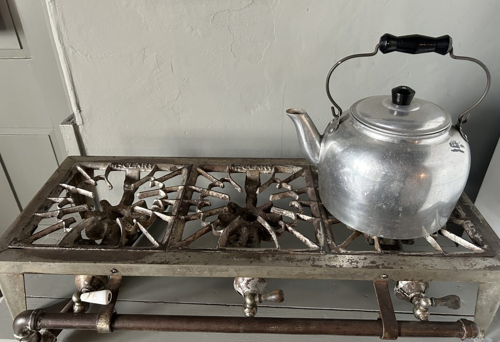 An image of a three section hotplate with a tea kettle on the right.
