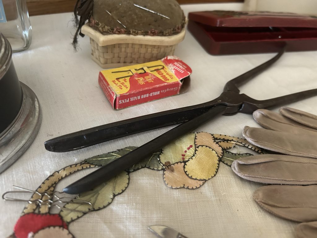 An image of iron curling tongs on a dressing table. Surrounding it are gloves, cuticle items, bobby pins and more.