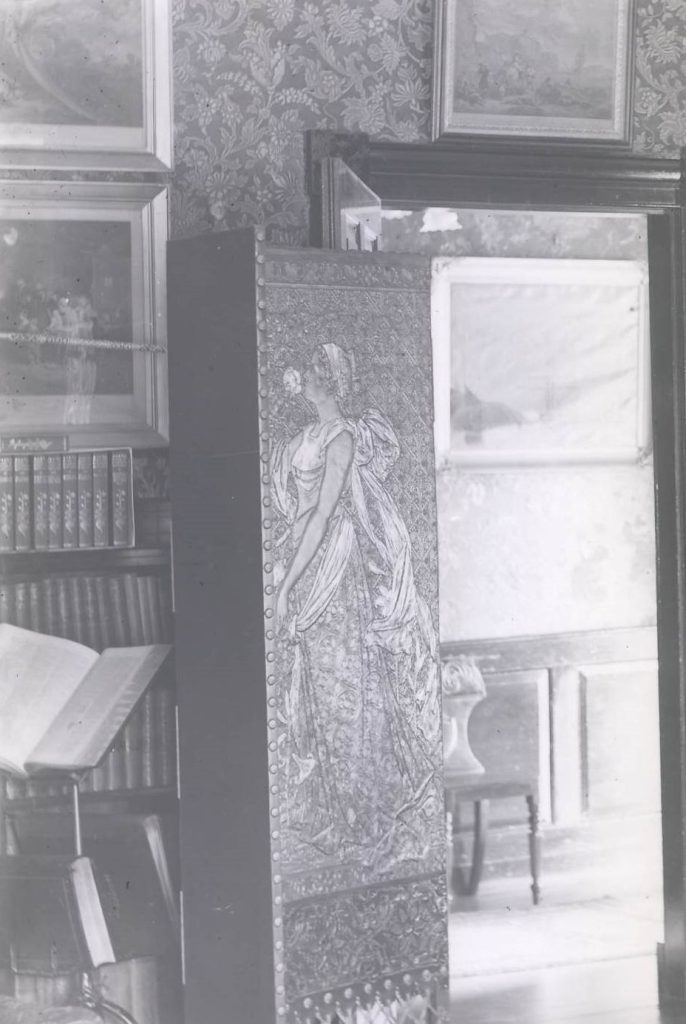 A black and white image of a room near a door opening. There is a large fire screen near the door