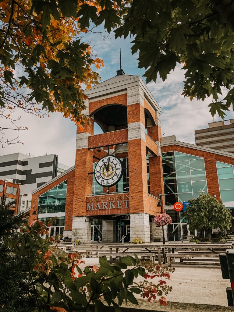 An image of a large red building with a clock face. In the front there are maple trees in the foreground of the image.