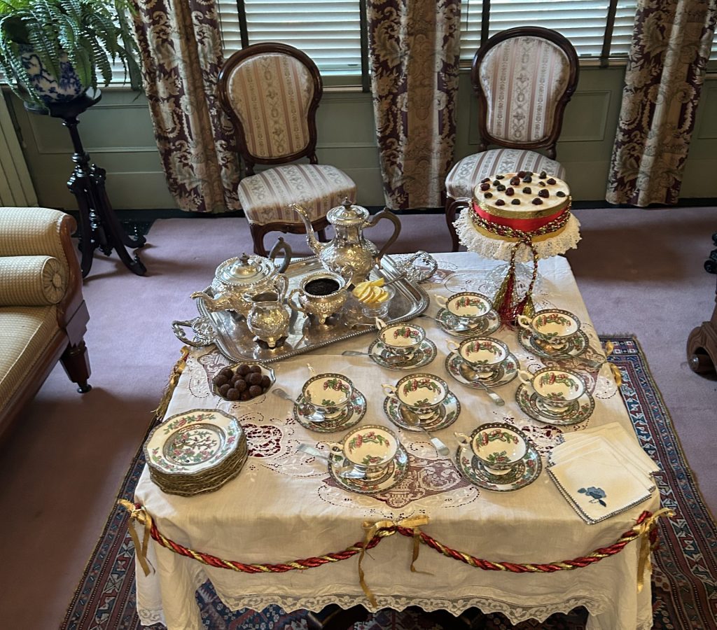 An image of a square table with a white tablecloth and India Tree Pattern teaset. Around the table there is a red bunting. In the background are two chairs.